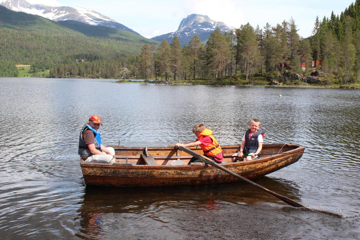 Tre barn i robåt på et vann, foto: Camilla Nesheim.