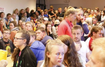 Mange unge mennesker står samlet i et rom.