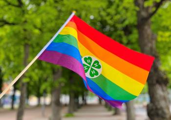 Pride-flagg med 4H-kløver. Trær i bakgrunnen