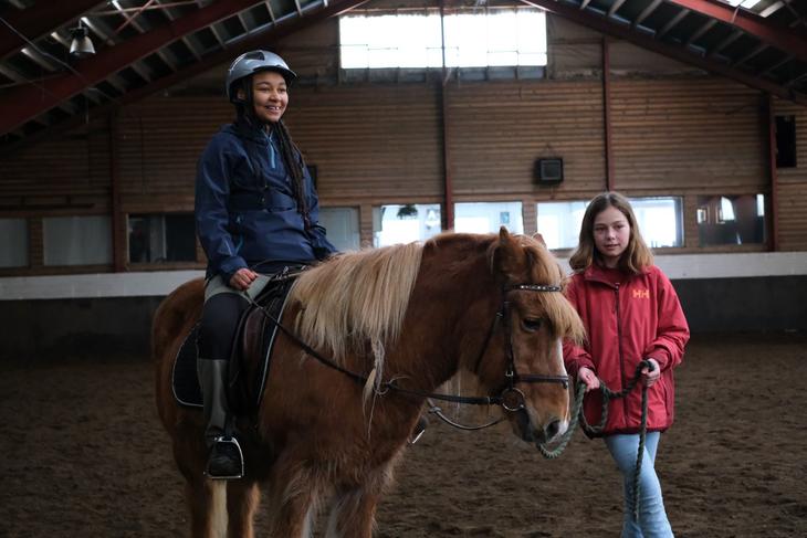 Ridehall, jente sitter på hest, annen jente holder hesten