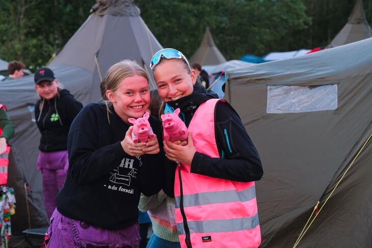 To jenter, står foran telt, holder hver sin rosa lekegris