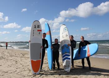 Medlemmar poserer med surfebrett på surfekurs