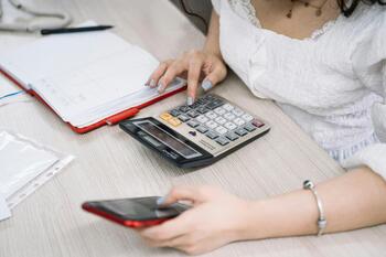 Kvinne med kalkulator, notatbok og mobil, foto: Anna Tarazevich (Pexels)